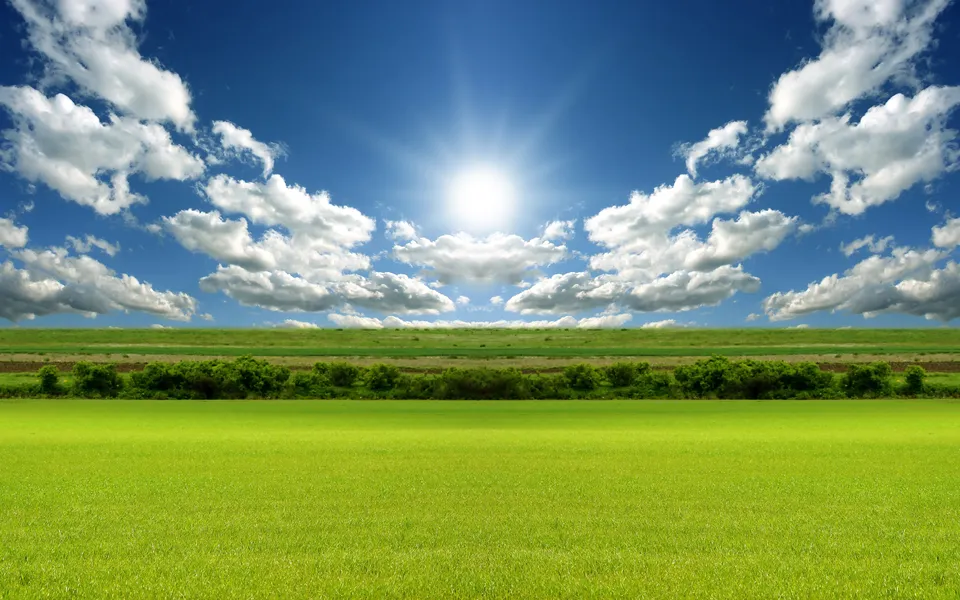 A bright sun shines in a blue sky with fluffy white clouds over a vibrant green field.