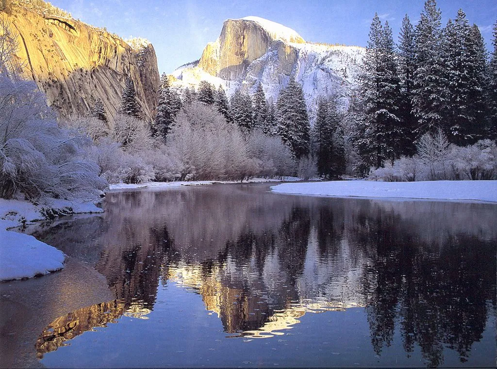A snow-covered valley with Half Dome mountain reflected in a calm river.