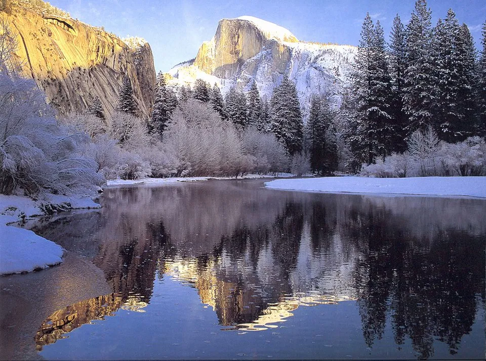 A snow-covered valley with Half Dome mountain reflected in a calm river.