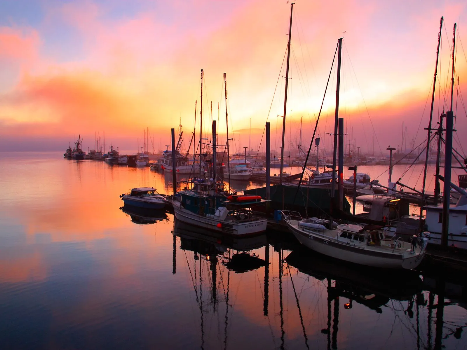 A harbor filled with boats reflects a vibrant orange and pink sunset sky.