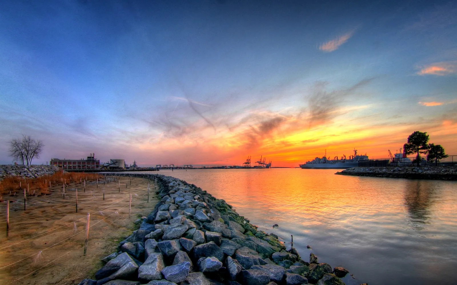 A colorful sunset over a harbor with ships and industrial buildings.
