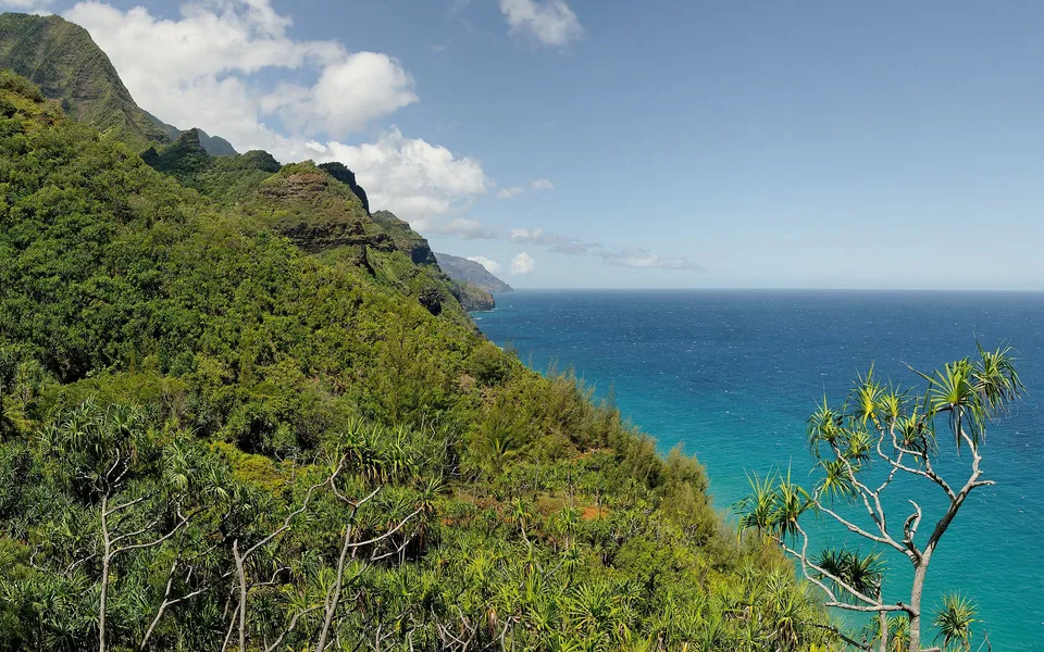 A view of lush green mountains meeting the vibrant blue ocean under a partly cloudy sky.