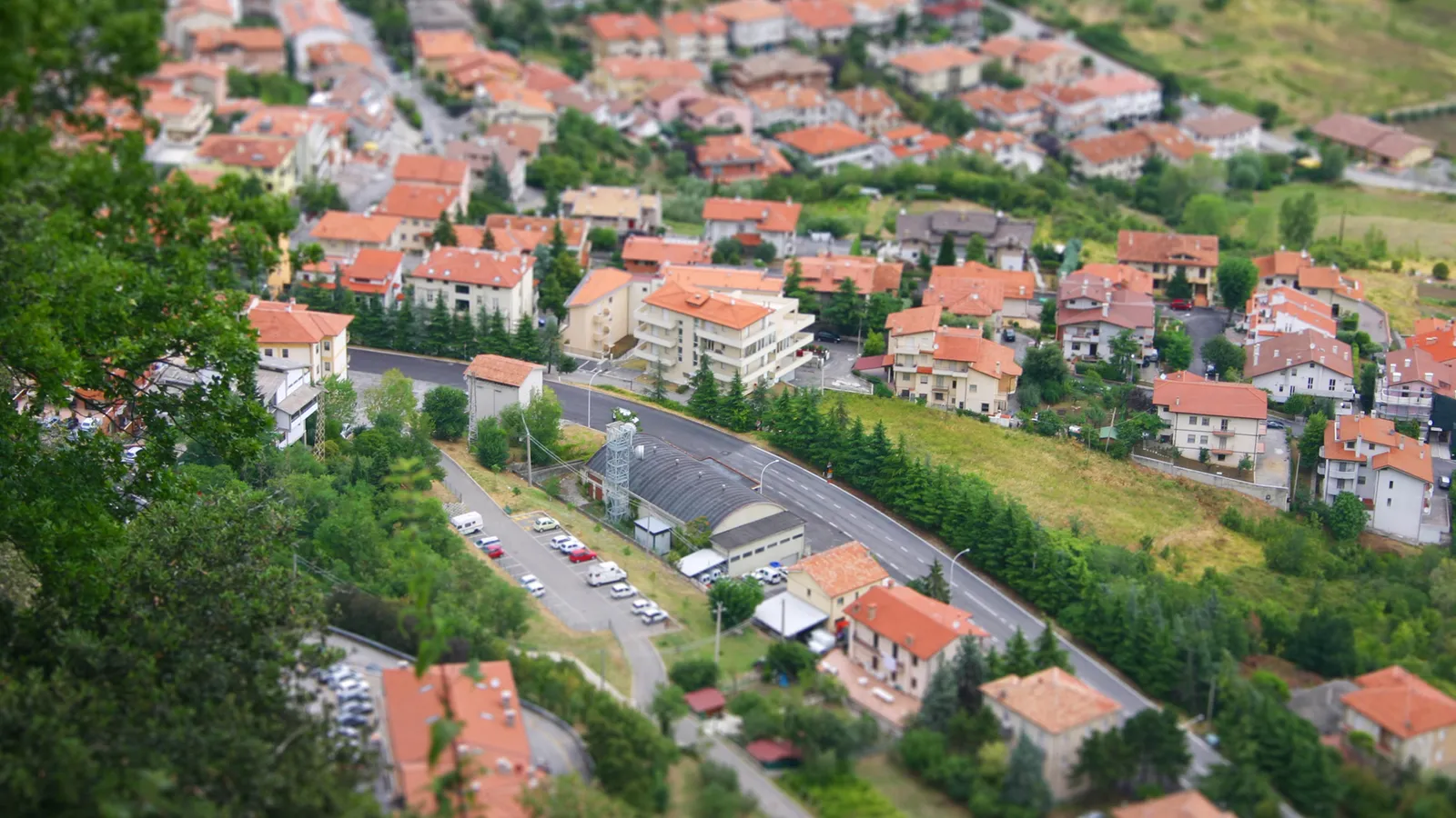 An aerial view of a town nestled on a green hillside, with many buildings featuring red tiled roofs.