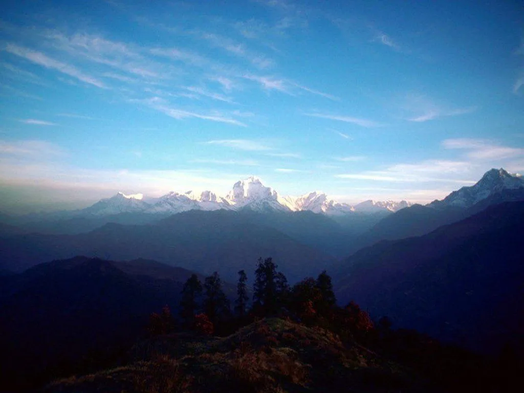 Distant snow-dusted Himalayan peaks are visible under a vast blue sky with thin, wispy clouds.