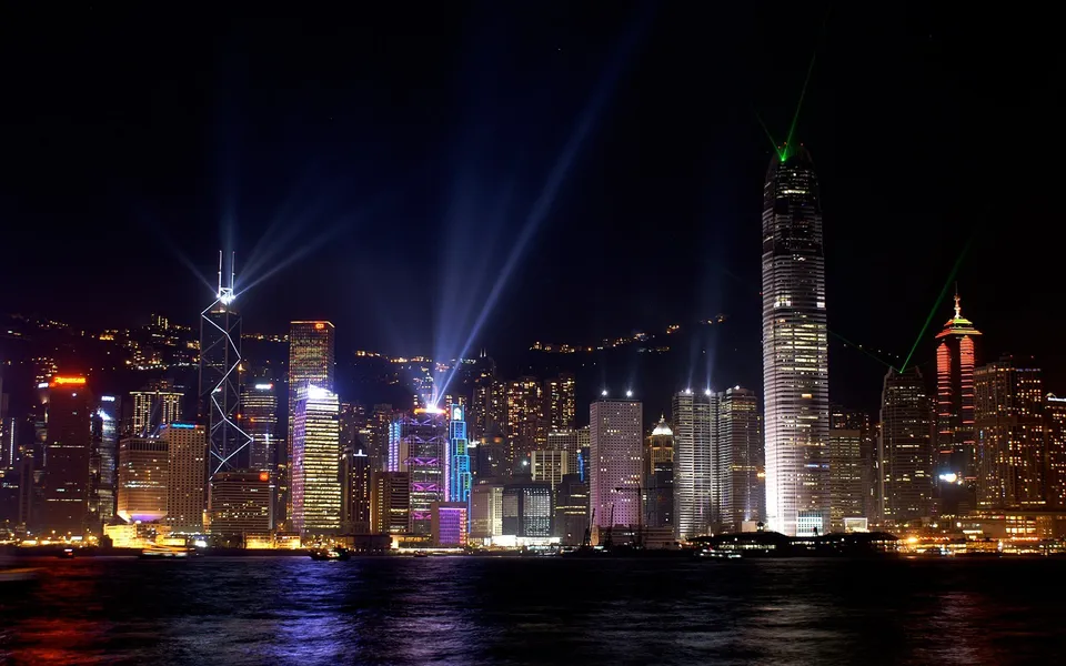 A vibrant city skyline at night, with illuminated skyscrapers and beams of light shooting into the dark sky.