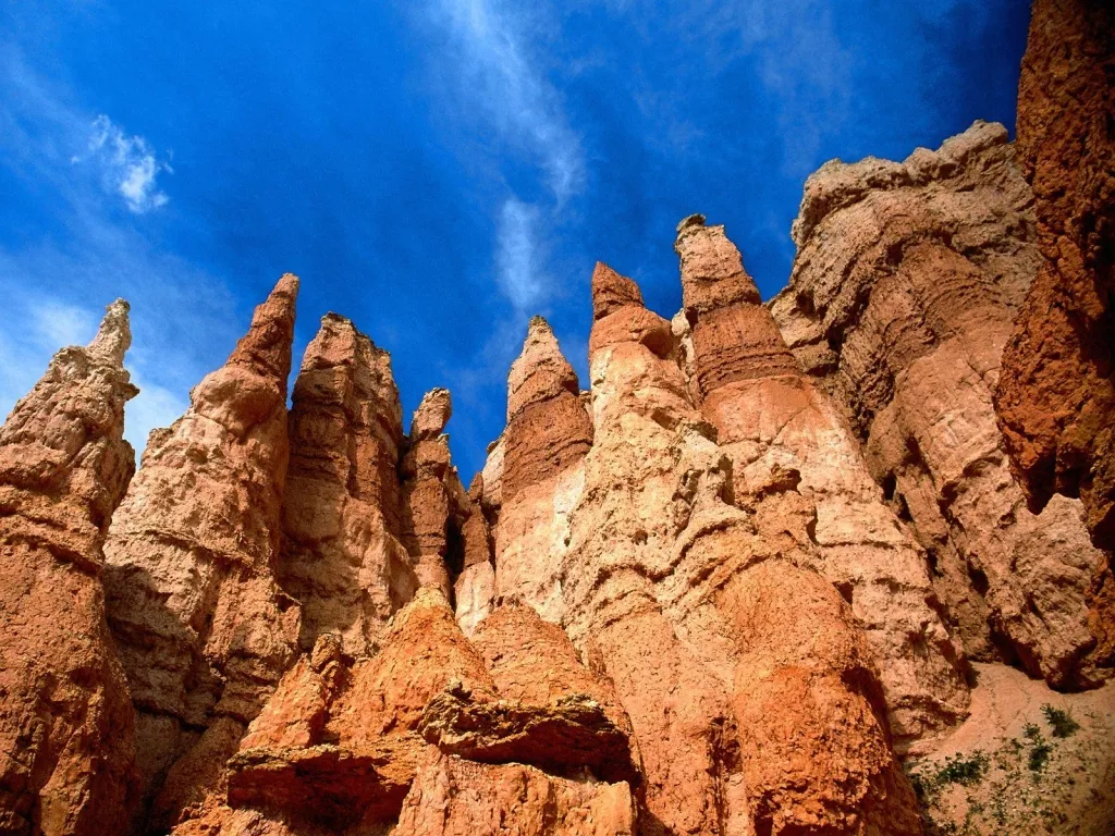 Tall, eroded sandstone hoodoos rise dramatically against a bright blue sky with wispy clouds.