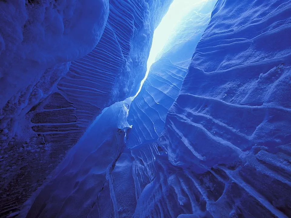Looking up through a narrow ice cave with sunlight filtering from above.