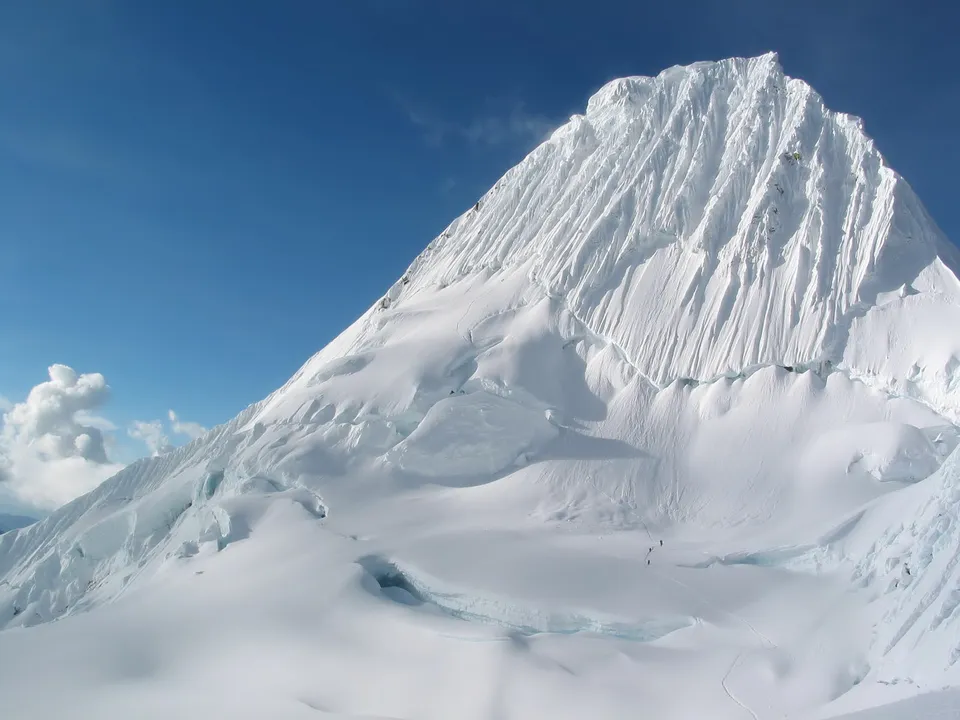 A vast, snow-covered mountain peak with intricate ice formations under a clear blue sky.