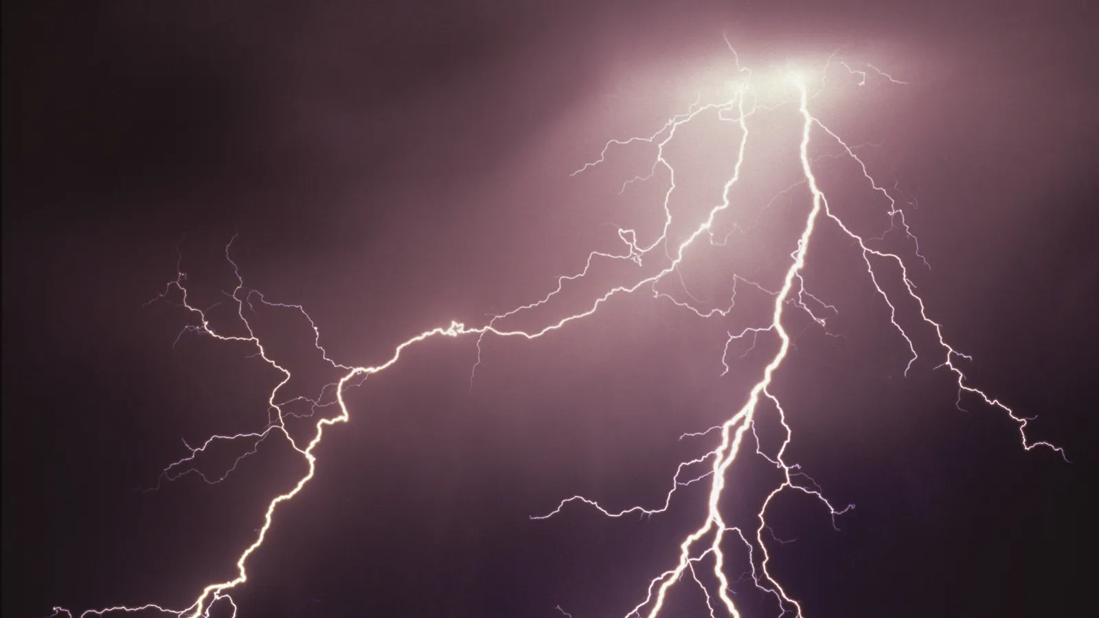 A dramatic lightning strike illuminates a dark, cloudy sky with brilliant white light, showing multiple branches.