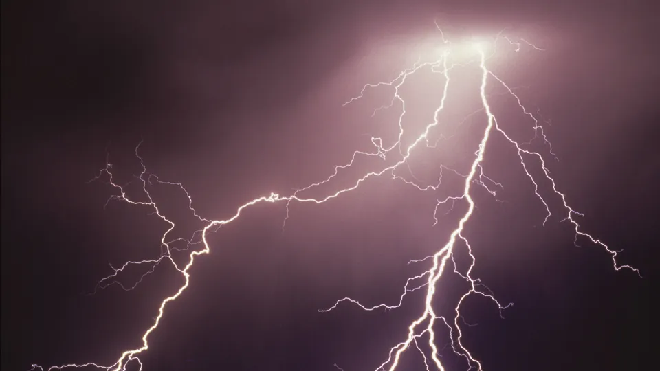 A dramatic lightning strike illuminates a dark, cloudy sky with brilliant white light, showing multiple branches.