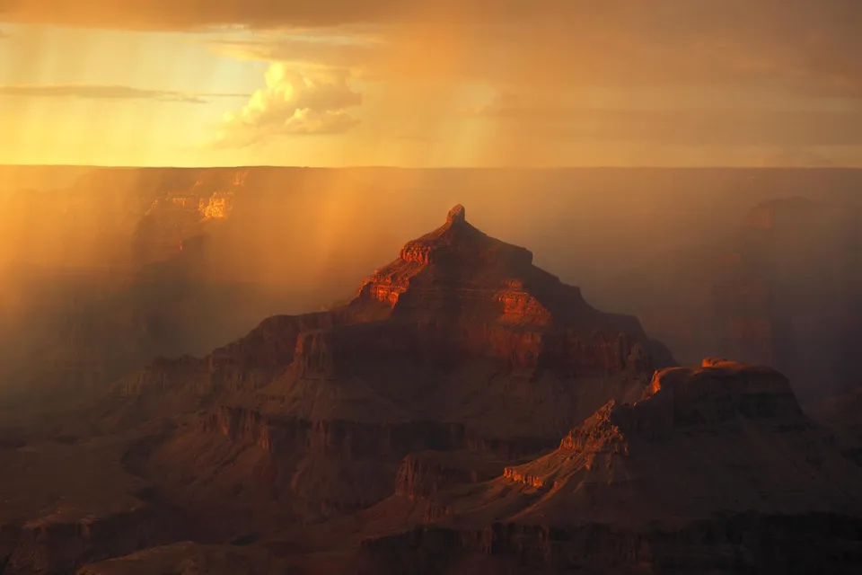 Sunbeams stream through hazy air onto the layered rock formations of the Grand Canyon at sunset.