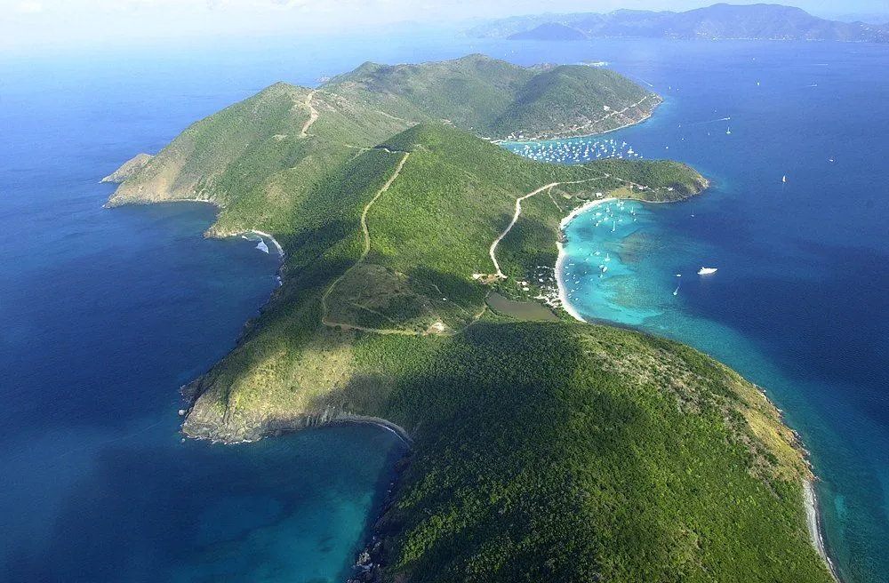 An aerial view shows a lush green island with bays dotted with sailboats and yachts.