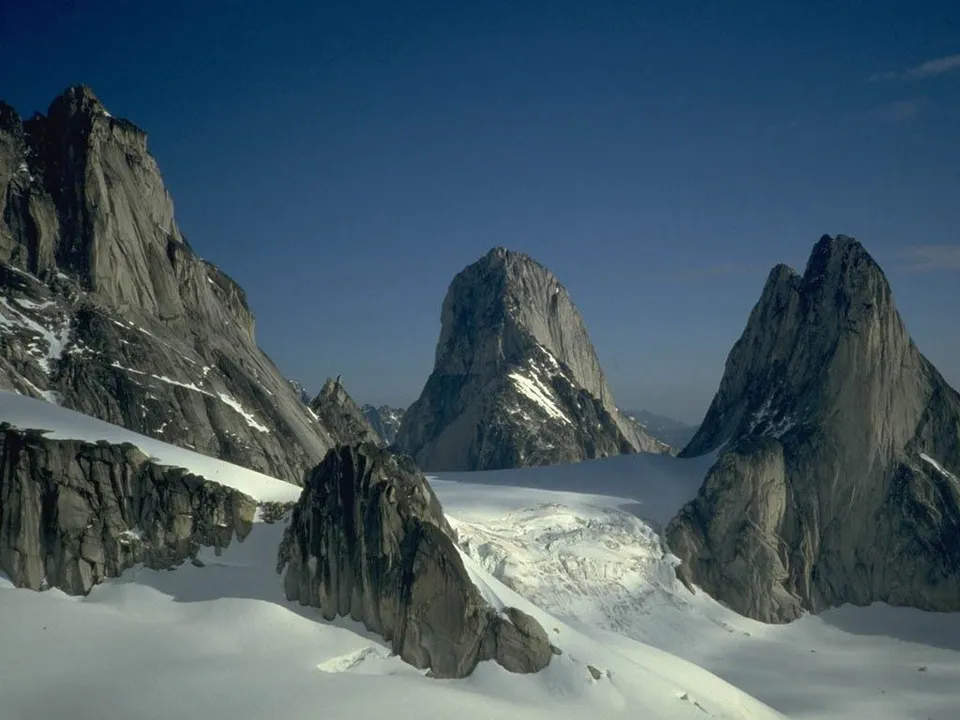Sheer granite mountain faces rise dramatically from a snow-covered landscape with a visible glacier.