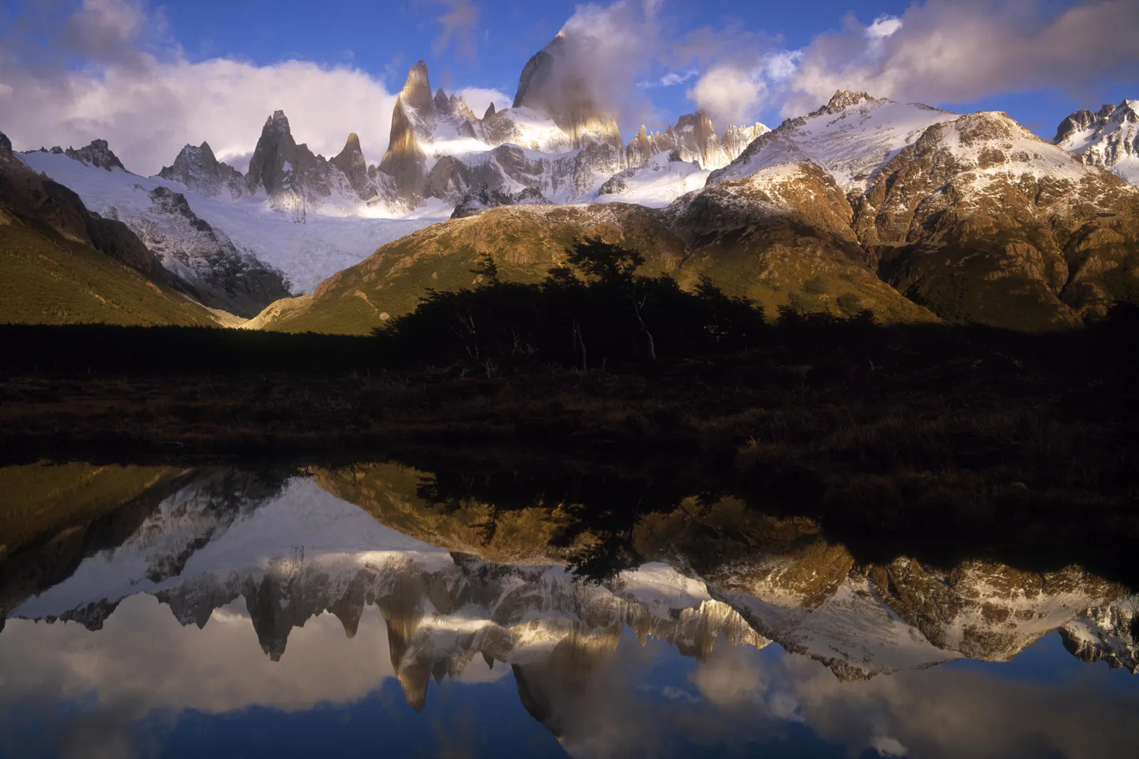 Jagged, snow-capped mountain peaks are reflected in the still water of a lake below.