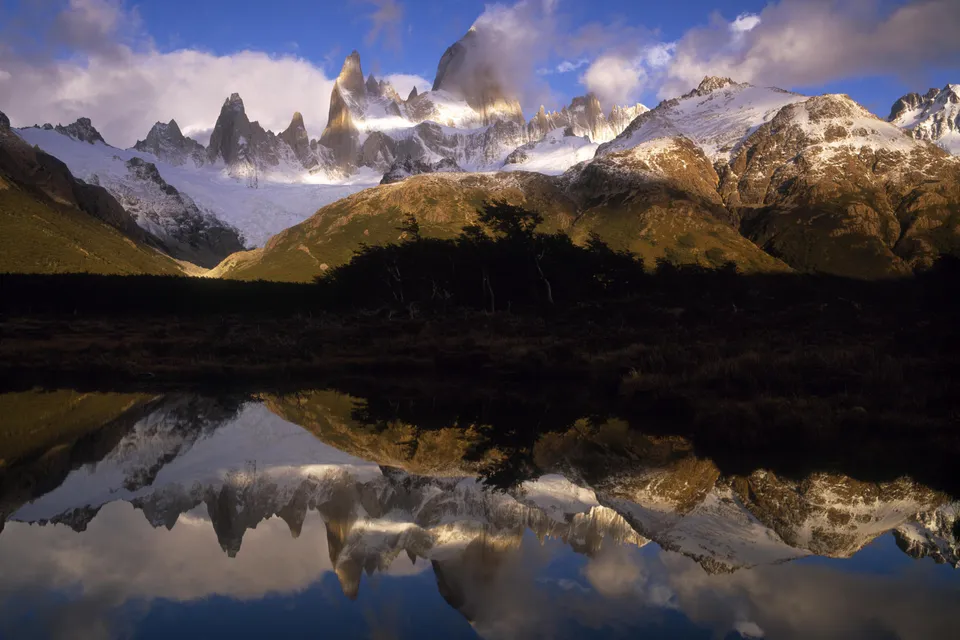 Jagged, snow-capped mountain peaks are reflected in the still water of a lake below.