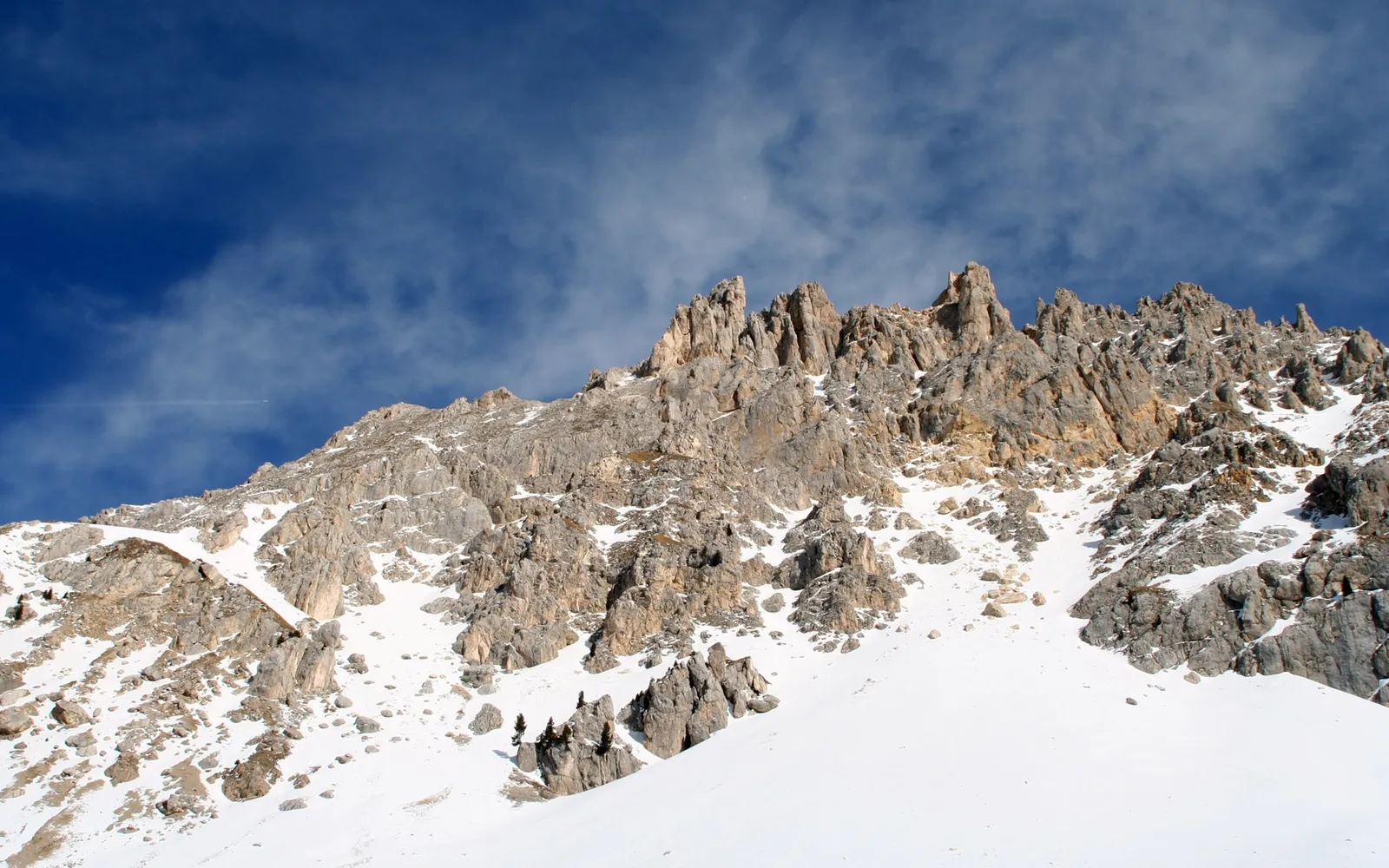 Sharp, rocky mountain peaks are dusted with snow against a deep blue sky with thin clouds.