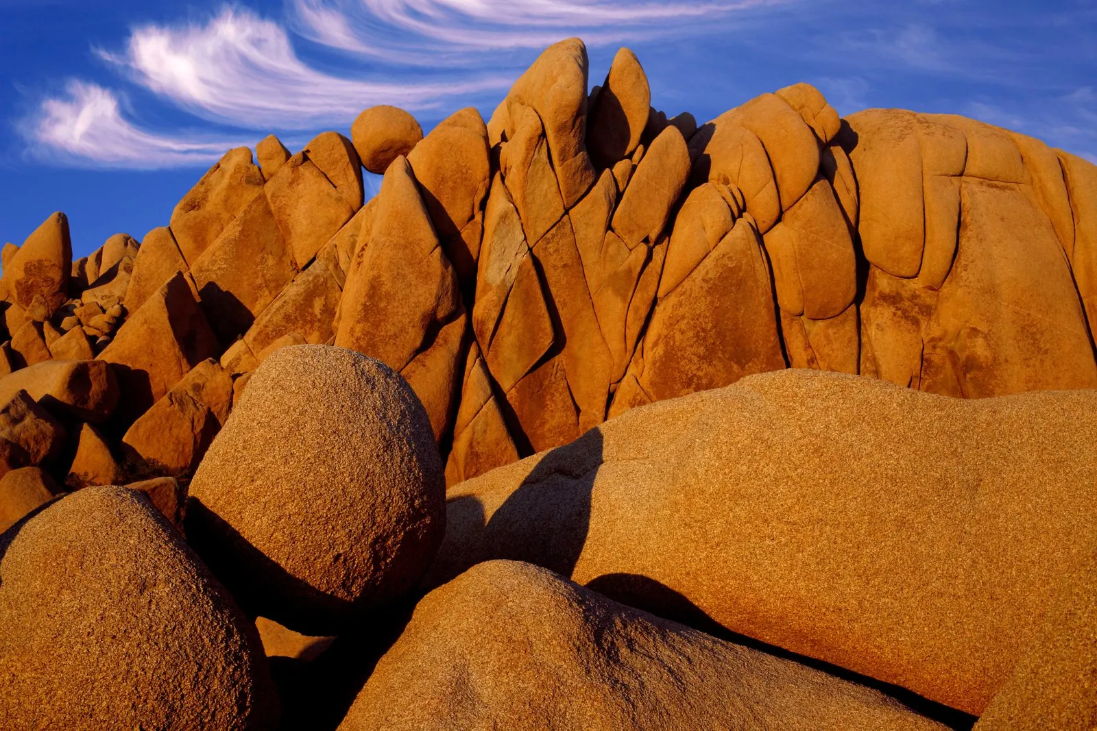 Large, rounded, and angular rock formations bathed in warm golden light under a blue sky with wispy clouds.