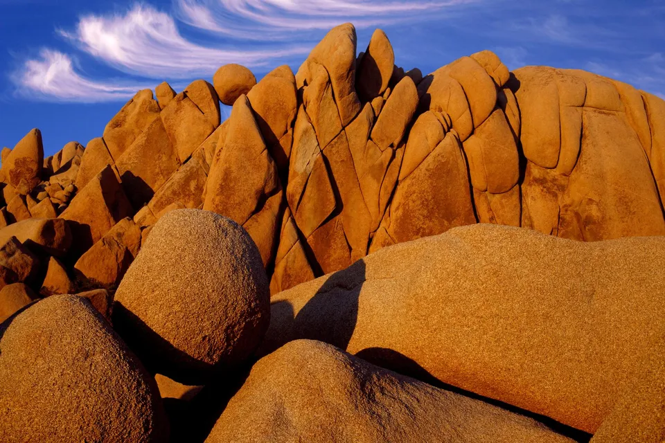 Large, rounded, and angular rock formations bathed in warm golden light under a blue sky with wispy clouds.