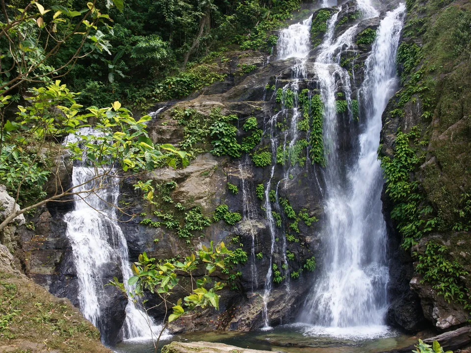 A multi-tiered waterfall cascades down a rocky cliff face covered in lush green vegetation.