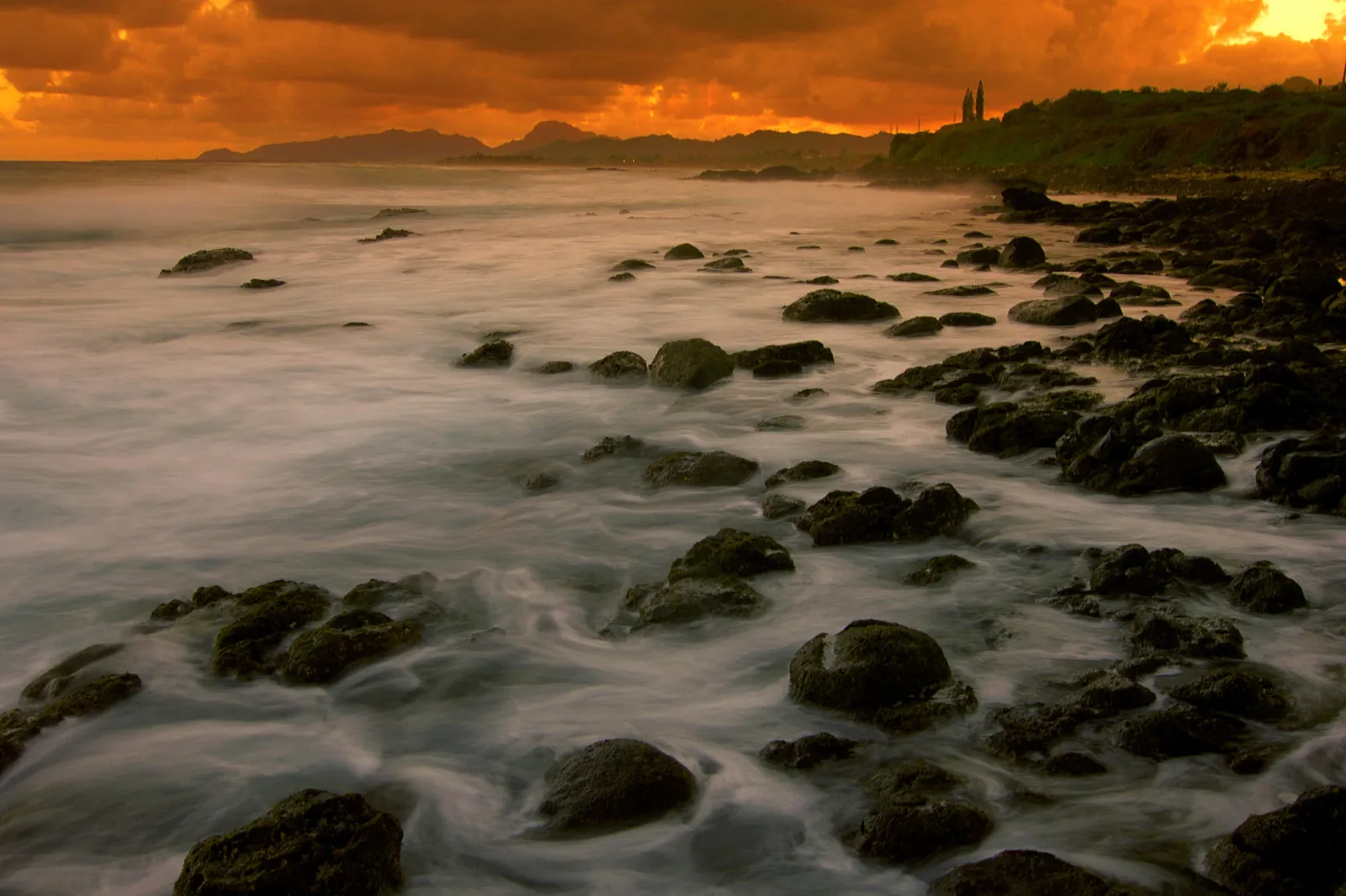 A dramatic sunset with orange clouds over a rocky coastline and the ocean.