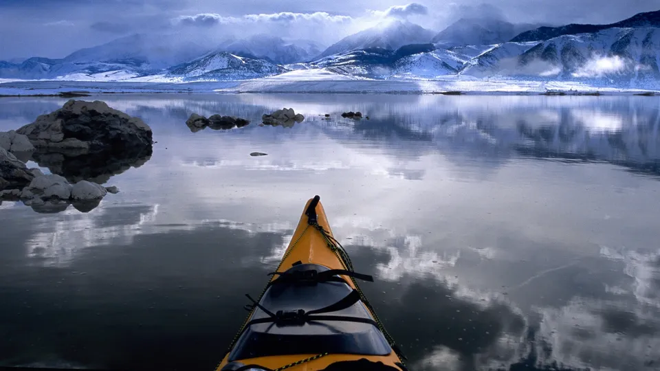 View from a yellow kayak looking out at a calm lake with snow-capped mountains in the background.