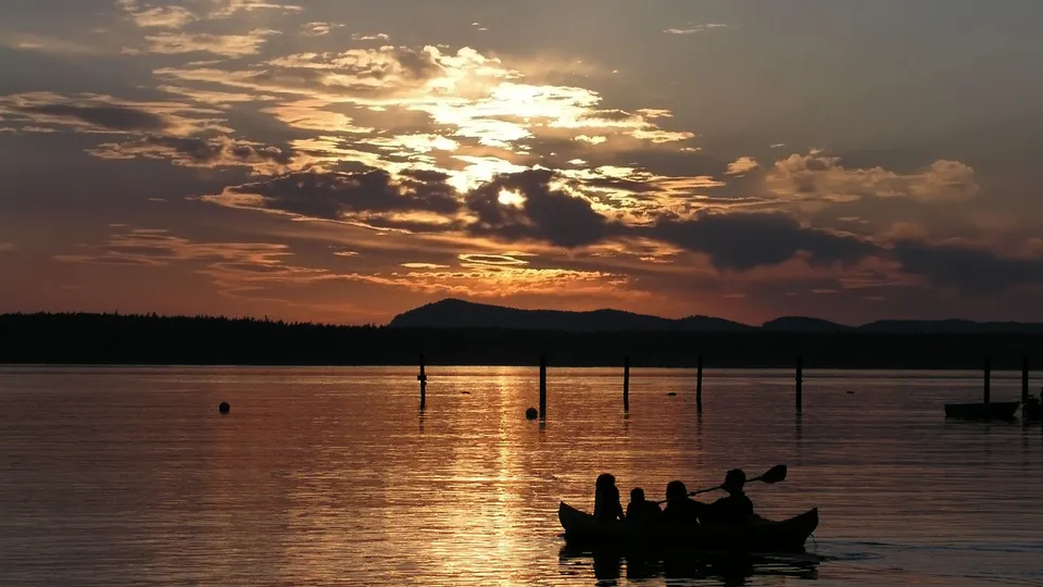 Silhouettes of people in a kayak on a lake at sunset, with golden light reflecting on the water.