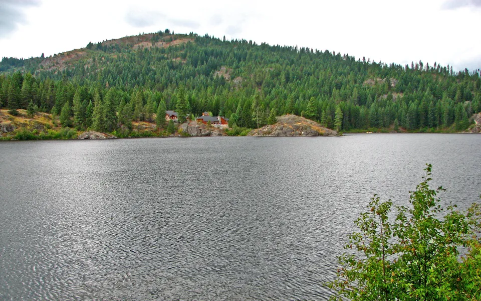 A wide lake with a forested hill in the background and houses nestled among the trees.