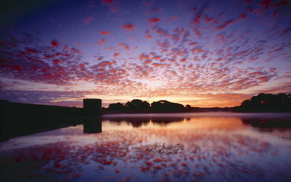 A vibrant sunrise paints the sky with pink and orange clouds reflected in a calm lake.