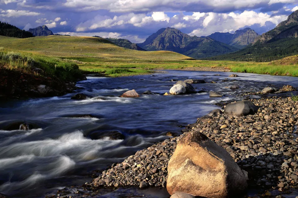 A wide river flows through Lamar Valley at dusk, with mountains in the background.