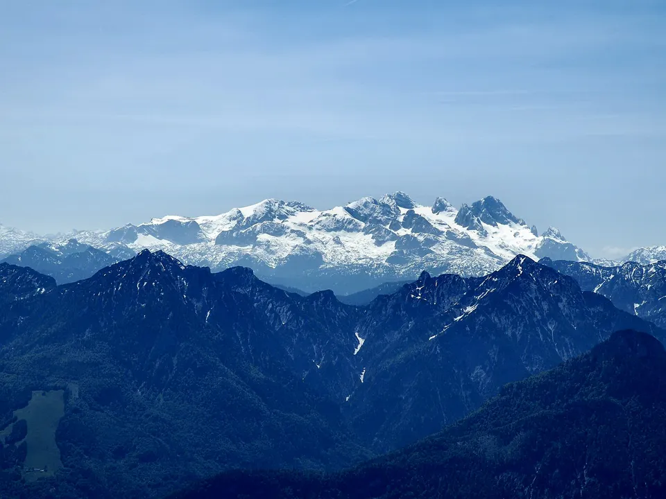 Multiple layers of mountain ranges recede into the distance, with the furthest peaks dramatically snow-capped.