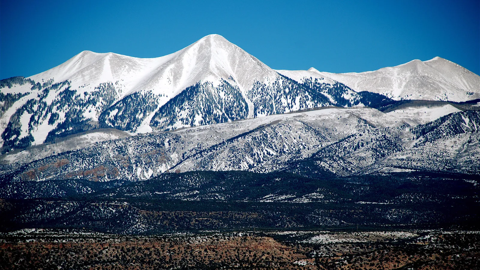 Layered mountain ranges show snow-covered peaks in the distance and dry, scrub-covered hills in the foreground.