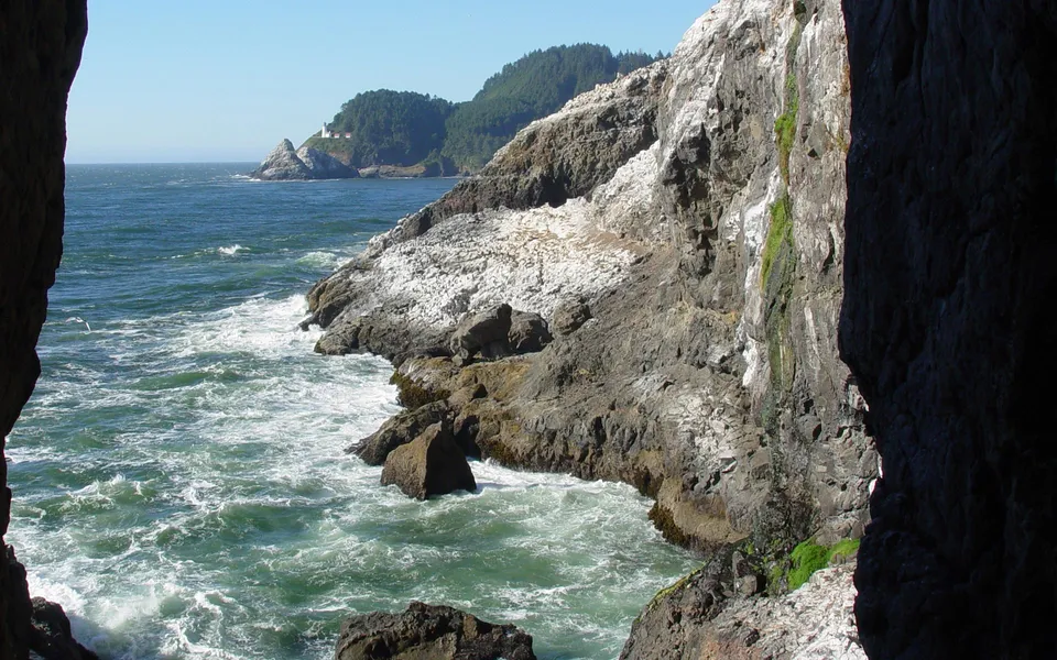 A lighthouse is visible on a distant headland above rugged coastal cliffs with waves crashing.