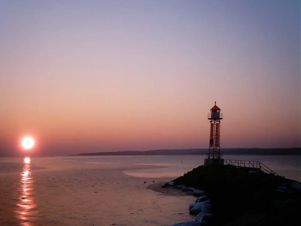 A lighthouse stands on a rocky outcrop by the sea during a vibrant sunset.