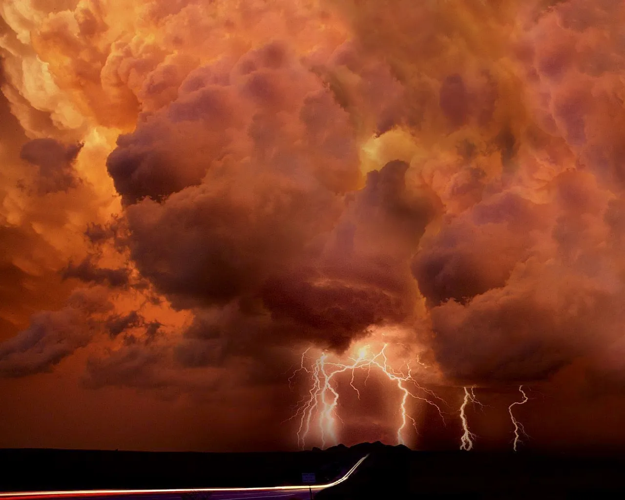 Multiple lightning bolts strike down from dramatic, fiery orange and red storm clouds over a dark landscape.