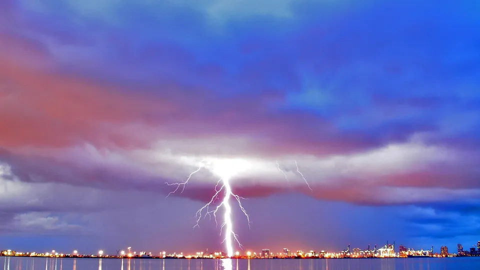 A bright lightning bolt strikes down from a stormy sky onto a city skyline at dusk.
