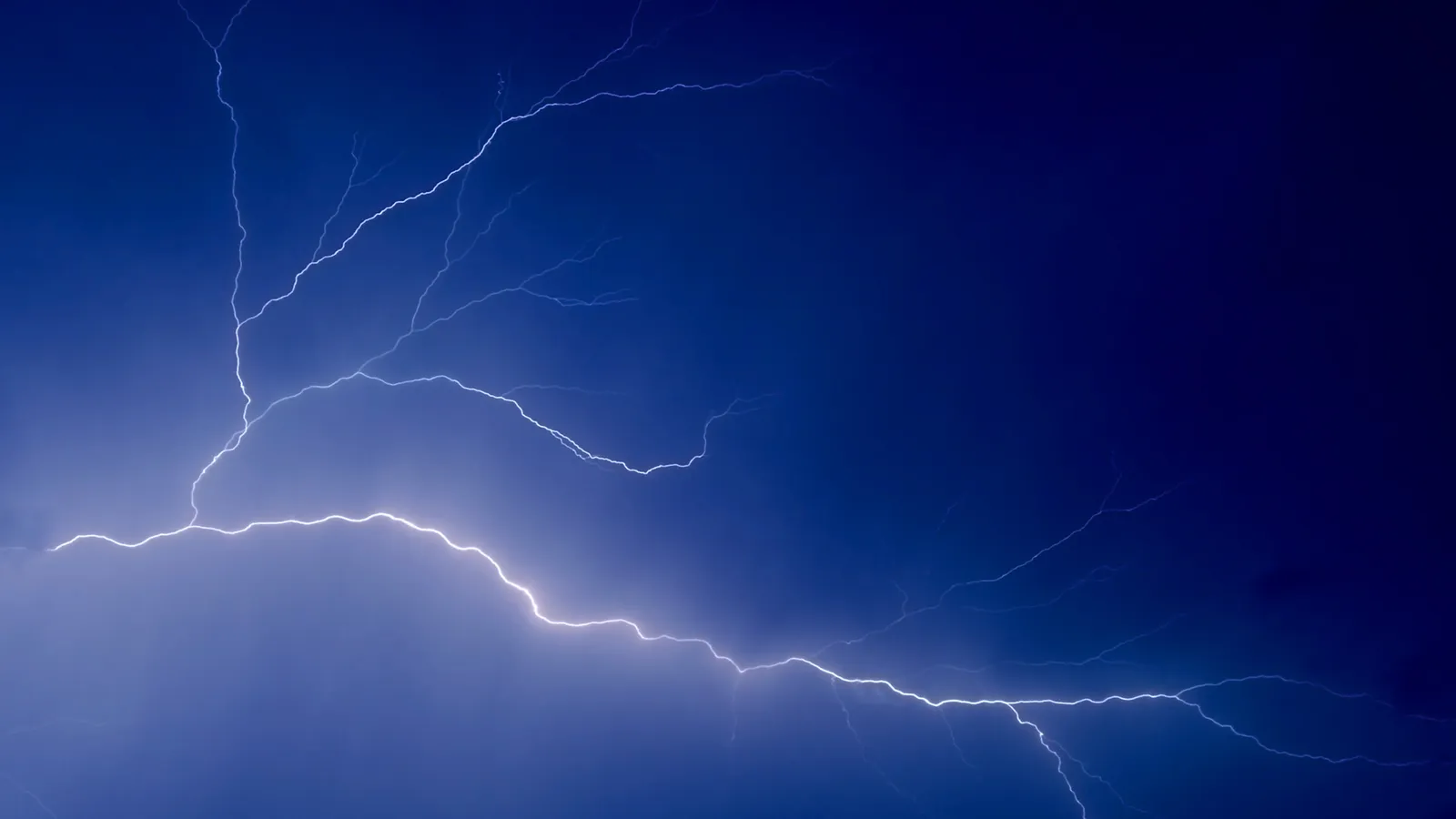 A bright white lightning bolt flashes across a deep blue sky.