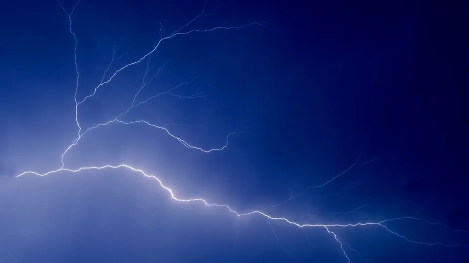 A bright white lightning bolt flashes across a deep blue sky.