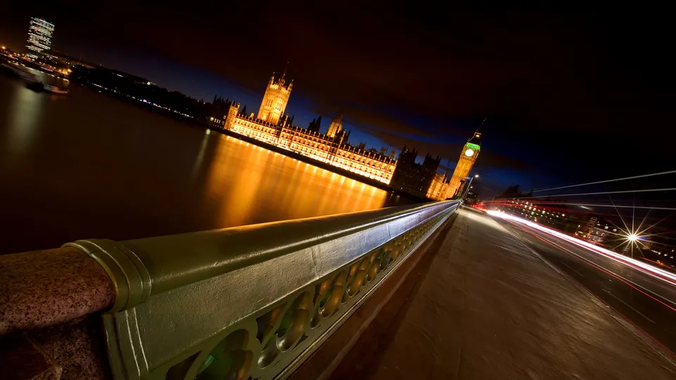 The Houses of Parliament and Big Ben illuminated at night, with light trails from traffic on a bridge.