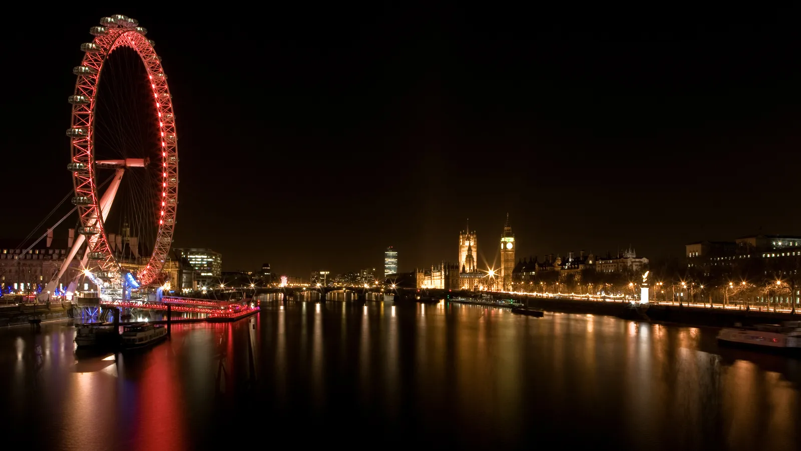 The London Eye and the Houses of Parliament illuminated at night, reflected in the River Thames.