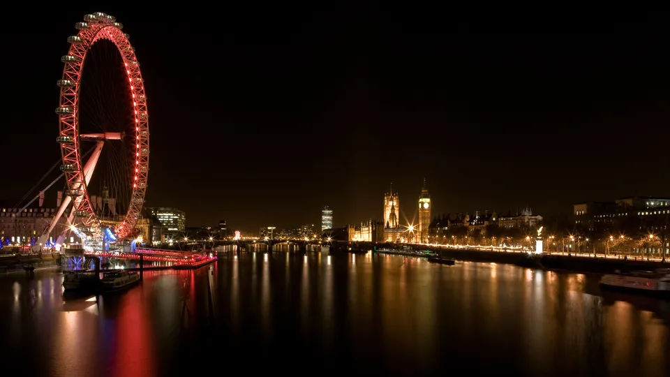 The London Eye and the Houses of Parliament illuminated at night, reflected in the River Thames.