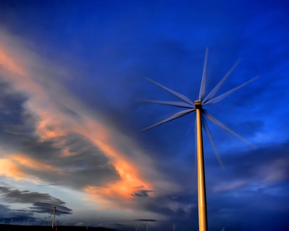 A single wind turbine with spinning blades against a dramatic blue and orange sunset sky.