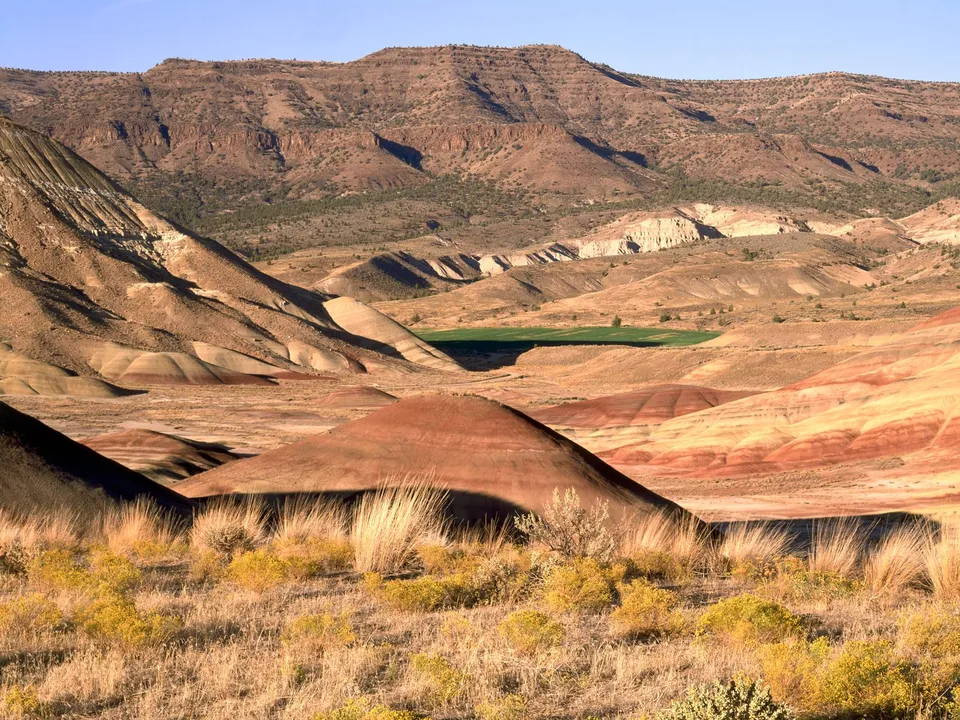 Sun casts long shadows across the colorful, layered hills of the Painted Hills in Oregon.