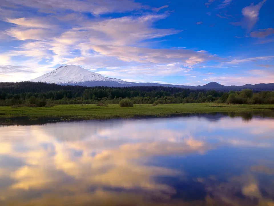 A snow-capped mountain is reflected in a calm lake during a colorful sunset.