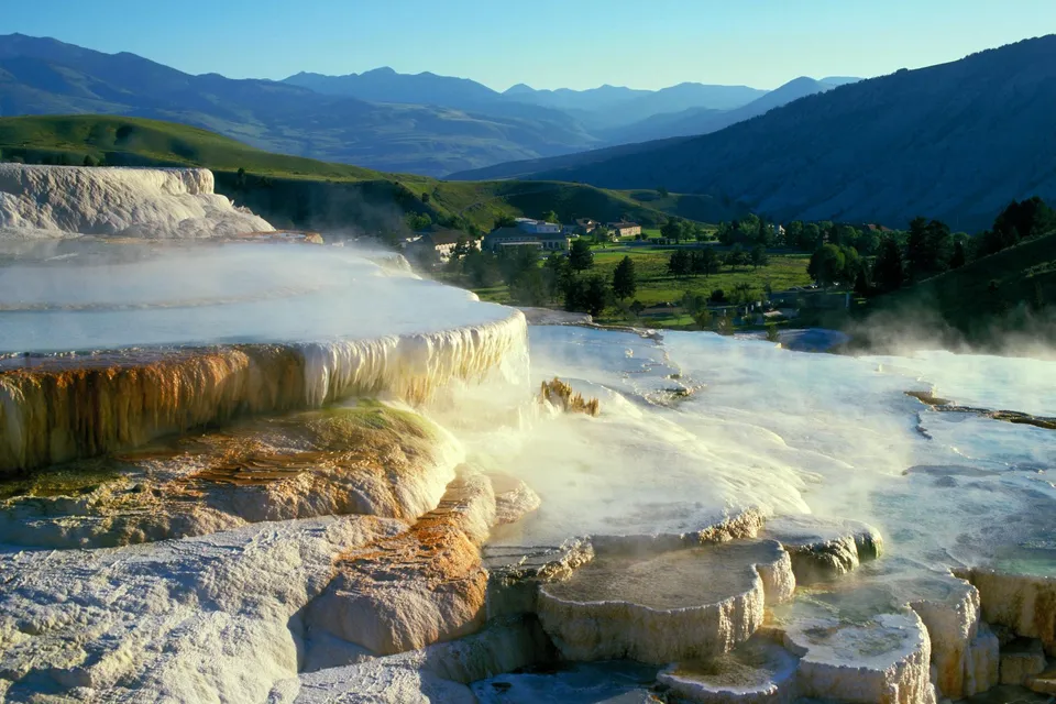 Steaming hot springs terraces with mineral deposits and distant mountains.