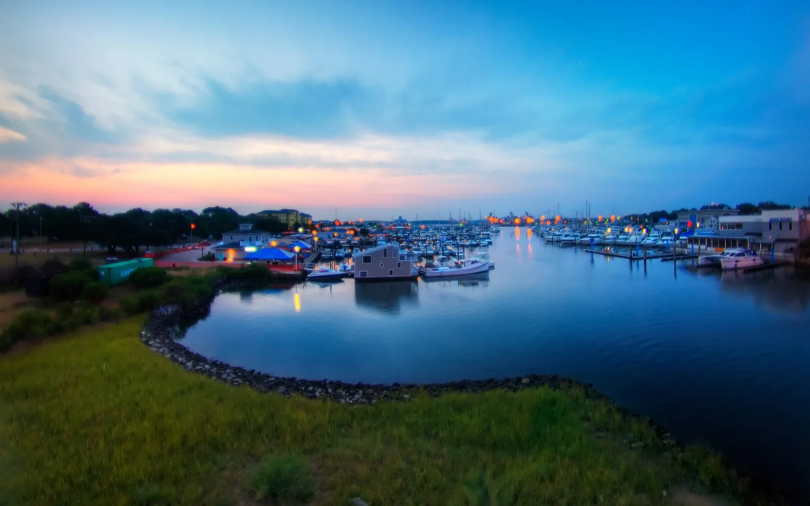 A wide view of a marina filled with boats at dusk, with a colorful sky and reflections on the water.