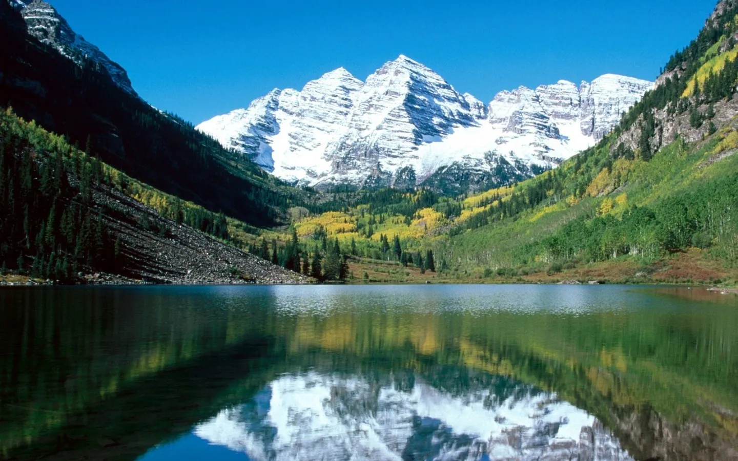Snow-capped Maroon Bells mountains reflected in the calm waters of Maroon Lake, surrounded by autumn foliage.