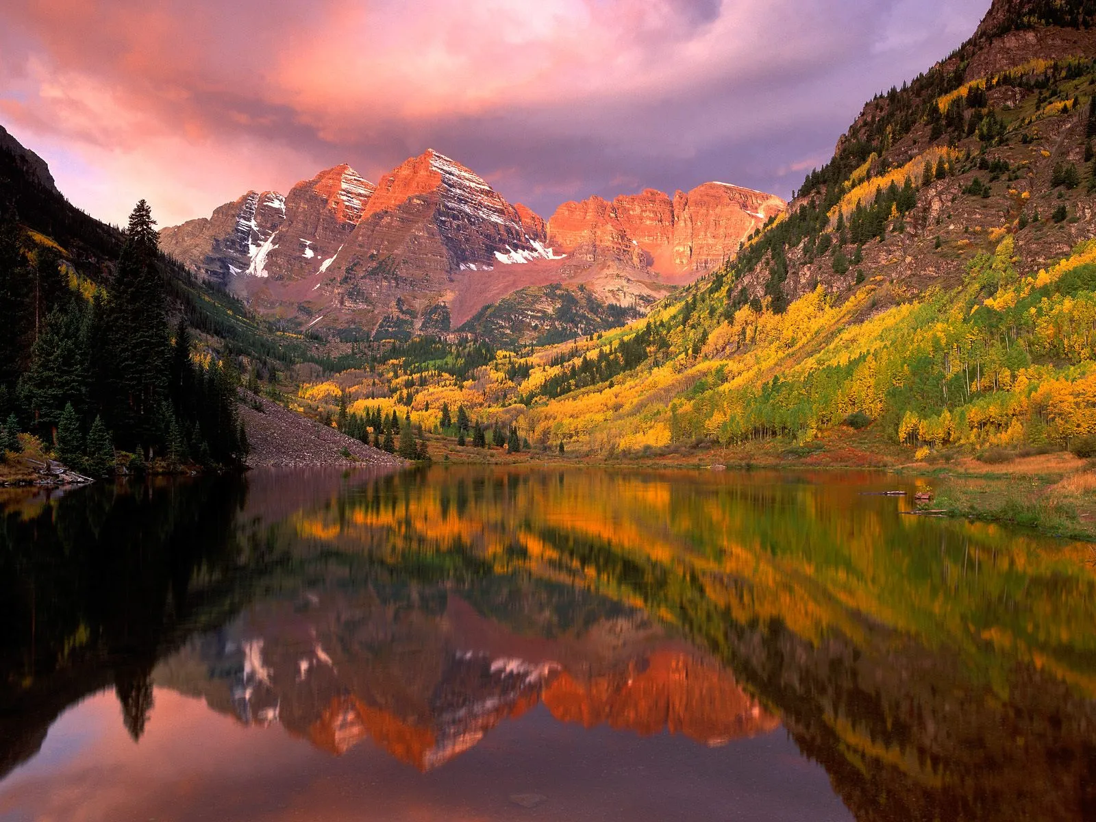 The Maroon Bells mountains are reflected in Maroon Lake during a colorful sunrise.
