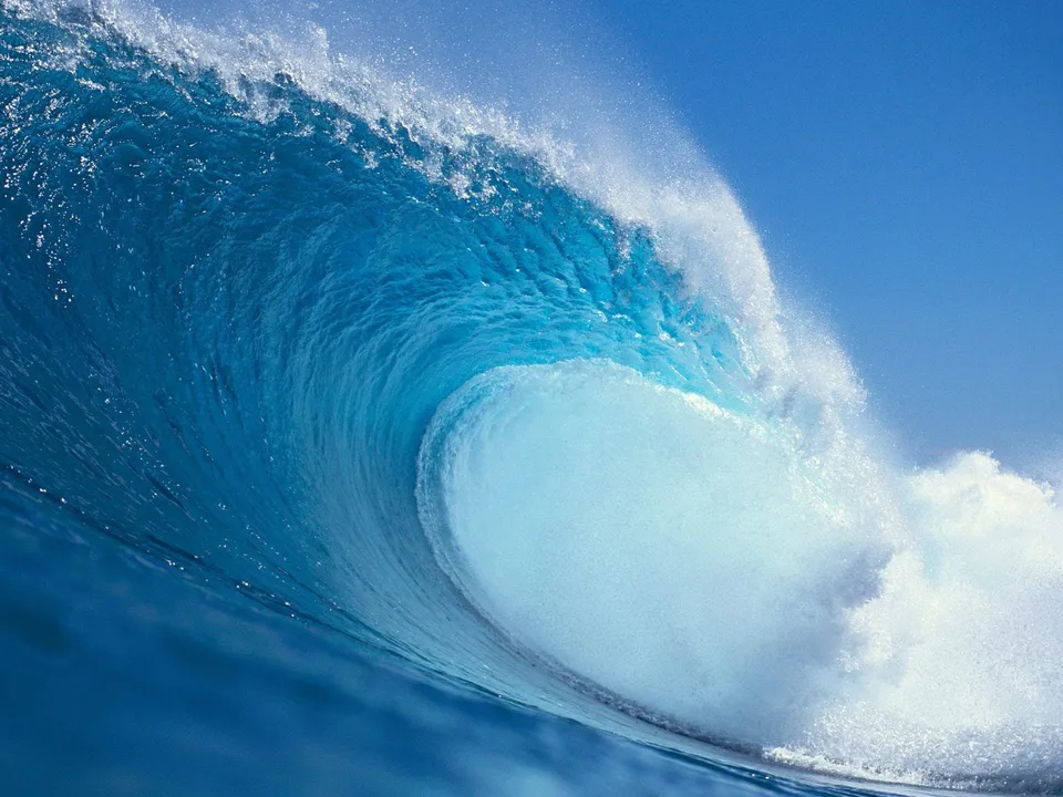 A massive ocean wave curls and breaks, its vibrant blue water contrasting with white foam.