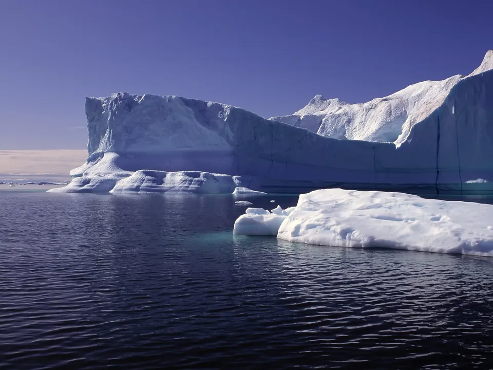 A massive iceberg casts shadows on the dark, rippling ocean water.