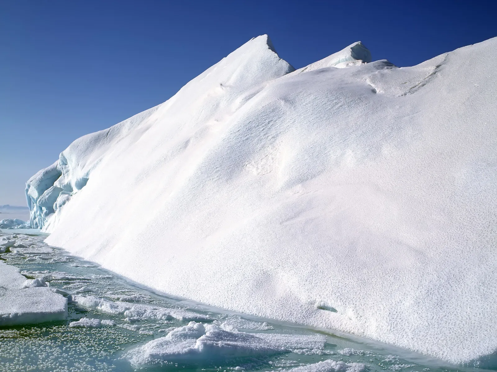 A massive iceberg with a snowy, textured surface and surrounding partially frozen water.